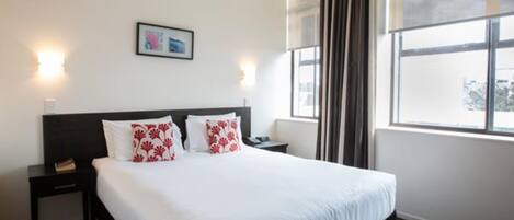 Una habitación de hotel con una cama grande, una mesita de noche y un cuadro en la pared, además de una ventana con cortinas.