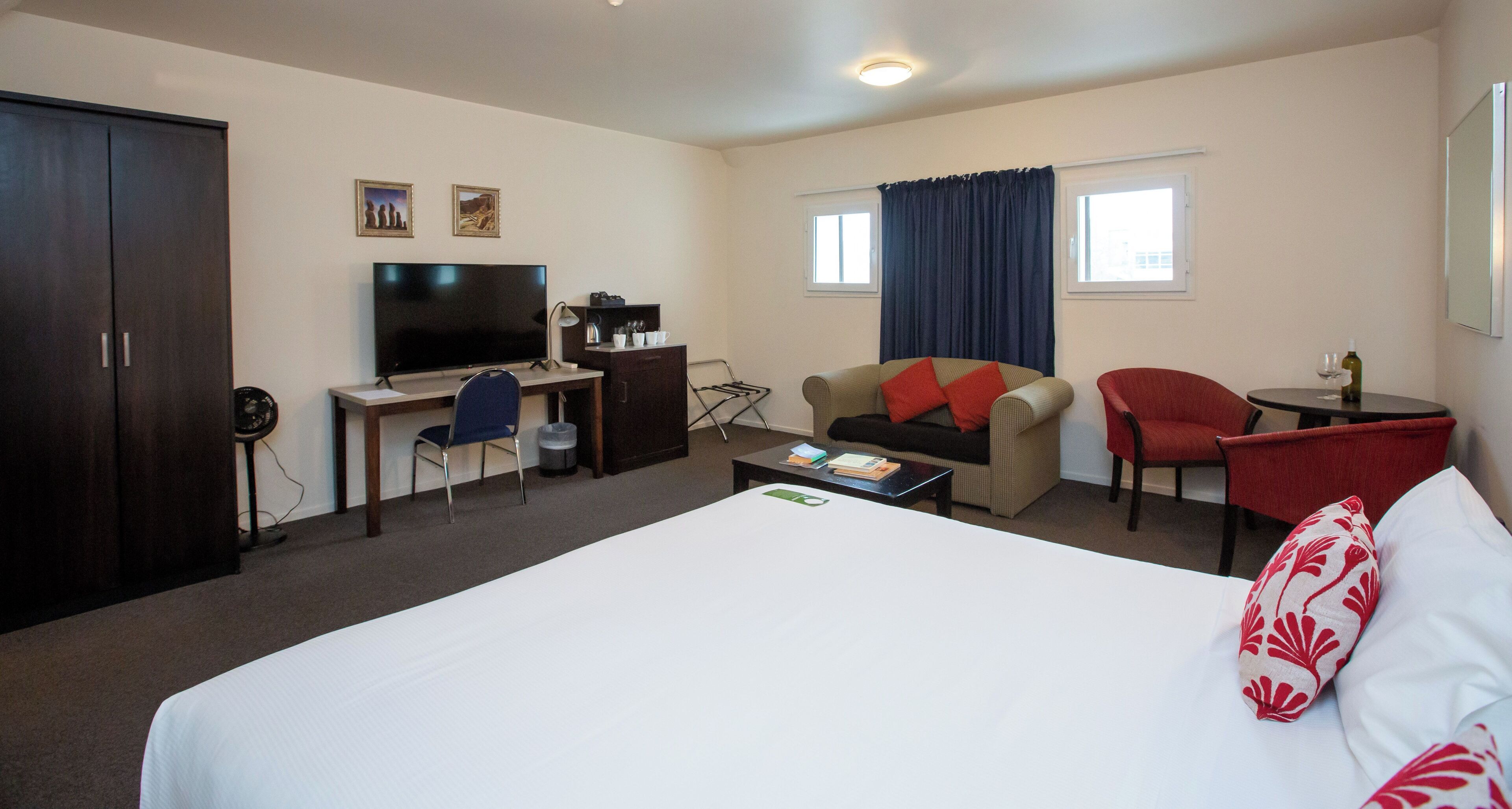 Een hotelkamer met een bed, een bureau met een televisie, een stoel, een bank en een kleine tafel met een fles wijn.
