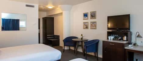 A hotel room with two beds, a desk with a TV, a chair, and a small table.