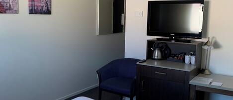 Habitación de hotel con cama, escritorio con televisor de pantalla plana, una silla, un armario pequeño y dos cuadros colgados en la pared.