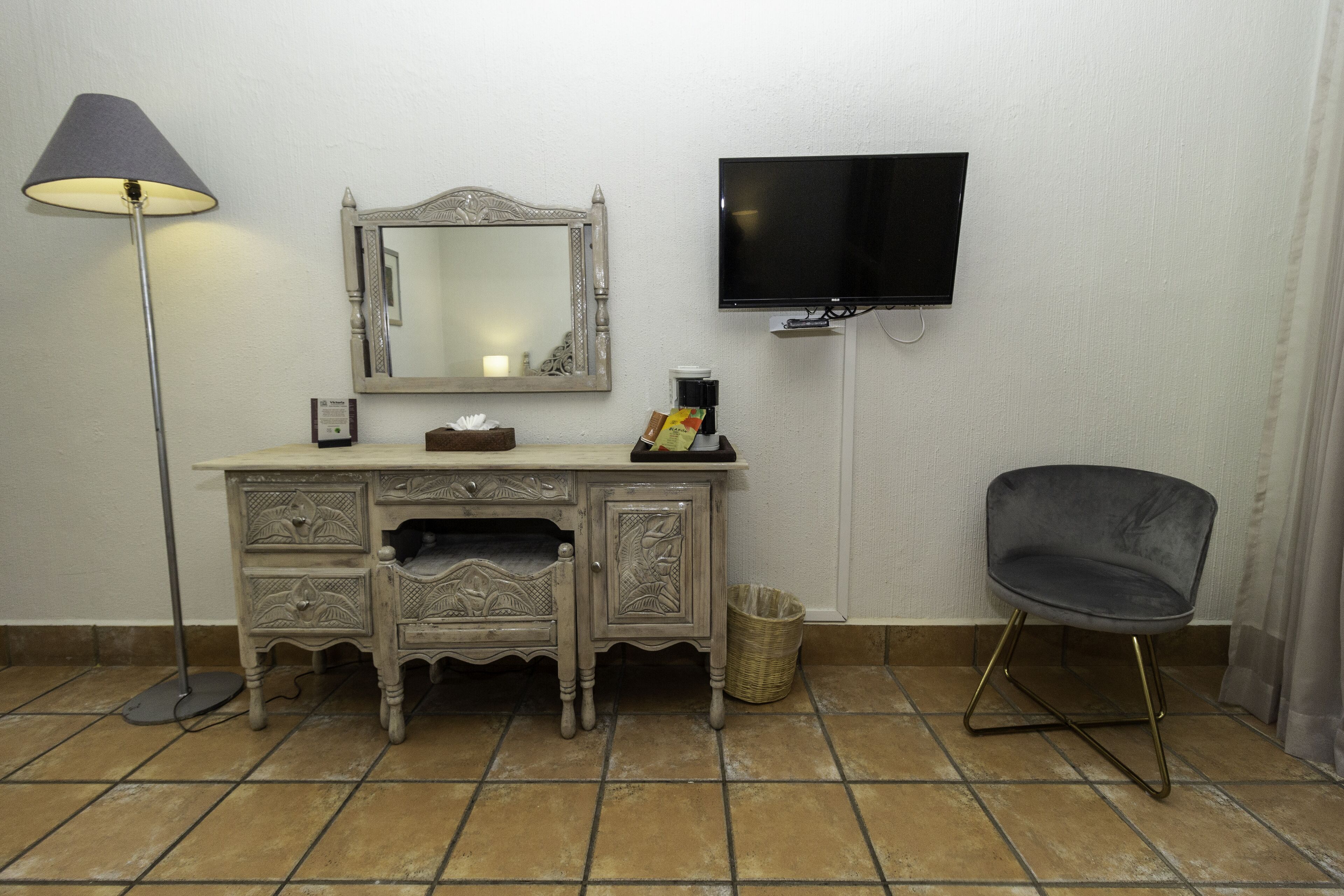 Una stanza con una cassettiera in stile vintage, una TV moderna, una lampada da terra e una sedia contemporanea.