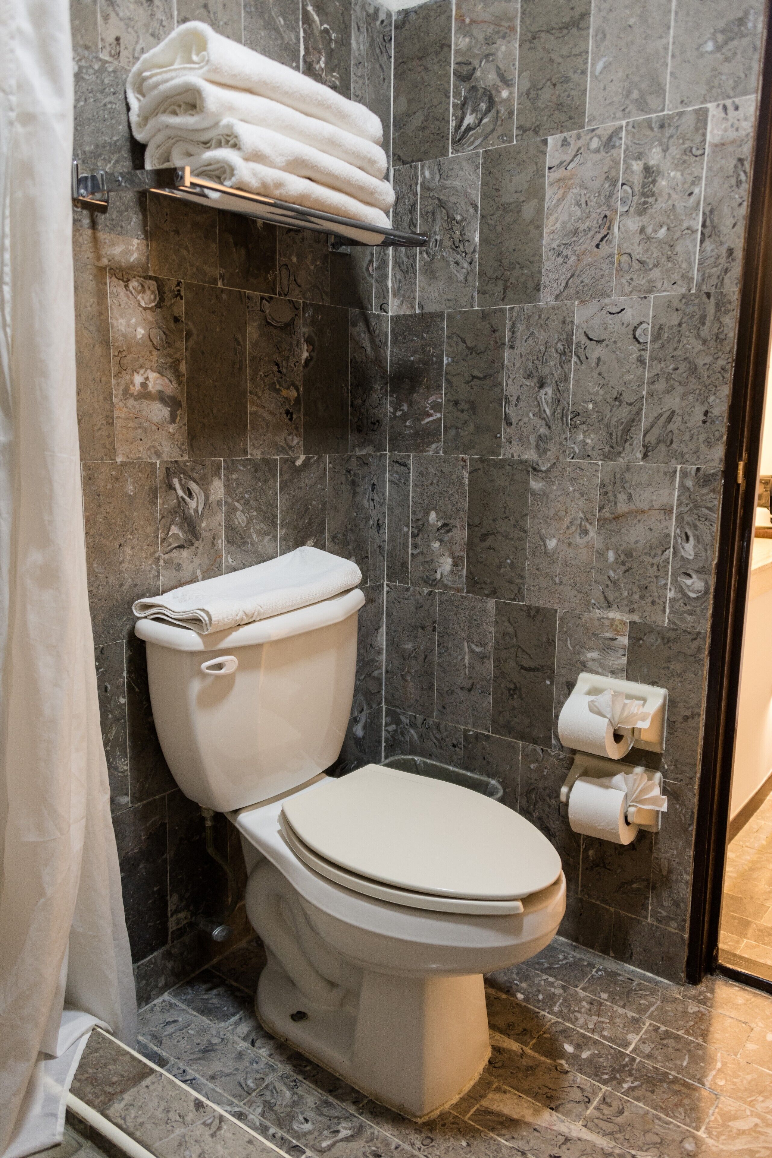 Ein Badezimmer mit Toilette, Marmorfliesen, einem Handtuchhalter mit gefalteten Handtüchern und einem Toilettenpapierhalter.