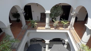 Un patio con columnas blancas, arcos, plantas en macetas y suelo de baldosas.