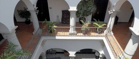 Un patio con columnas blancas, arcos, plantas en macetas y suelo de baldosas.