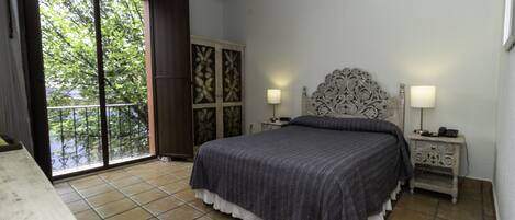 A bedroom with a bed, two bedside tables, a nightstand, a wardrobe, and a sliding glass door to a balcony.