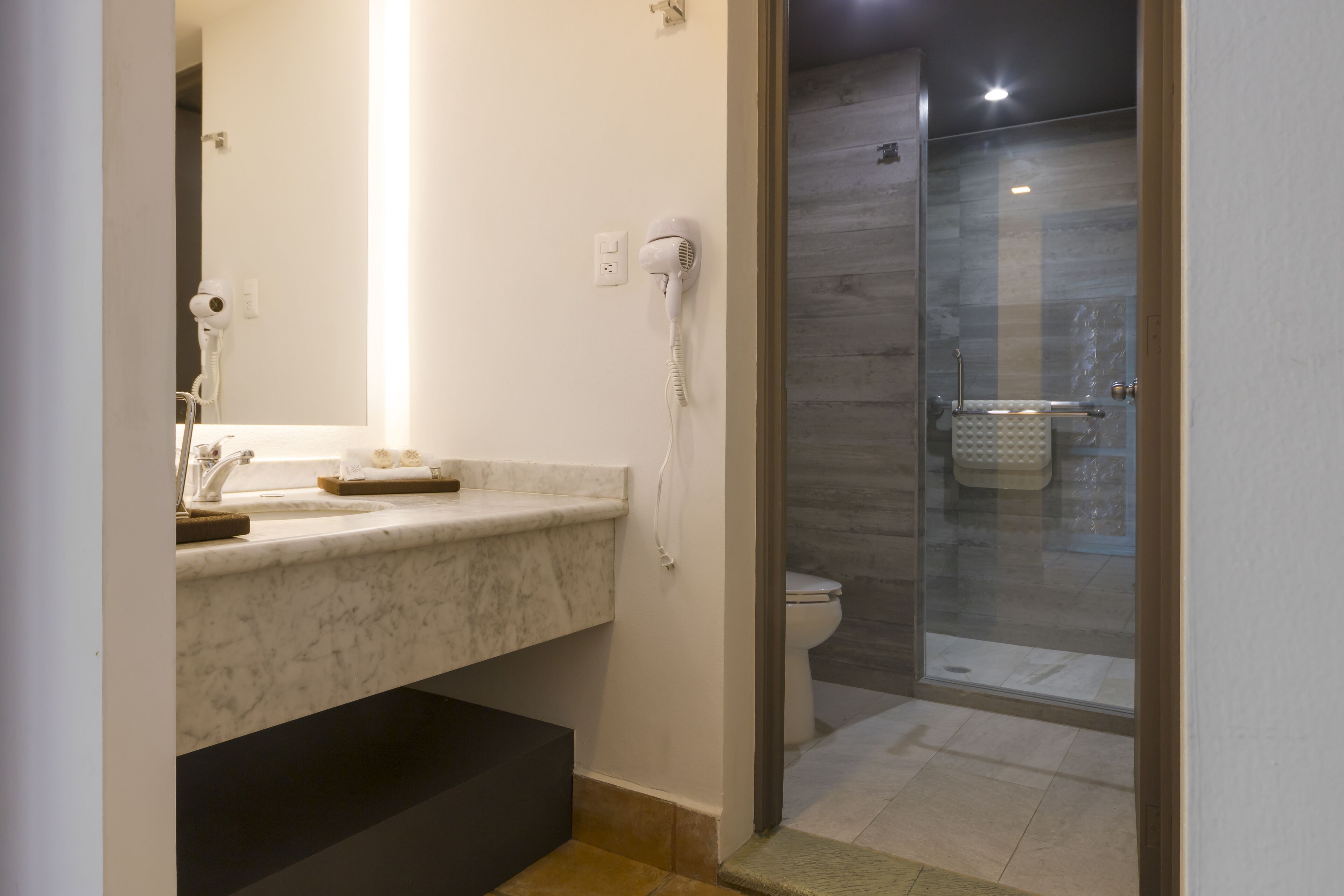 Un baño moderno con lavamanos de mármol, un secador de pelo y una cabina de ducha de vidrio.