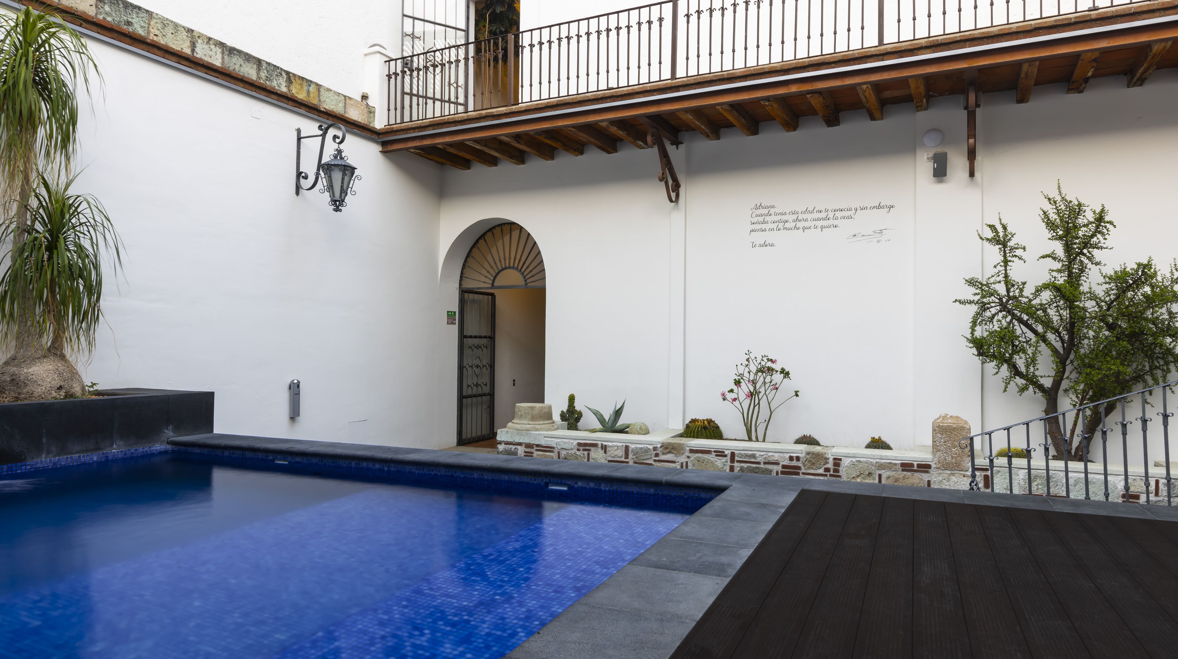 Un área de piscina con cubierta de madera, pared de piedra y barandilla metálica.