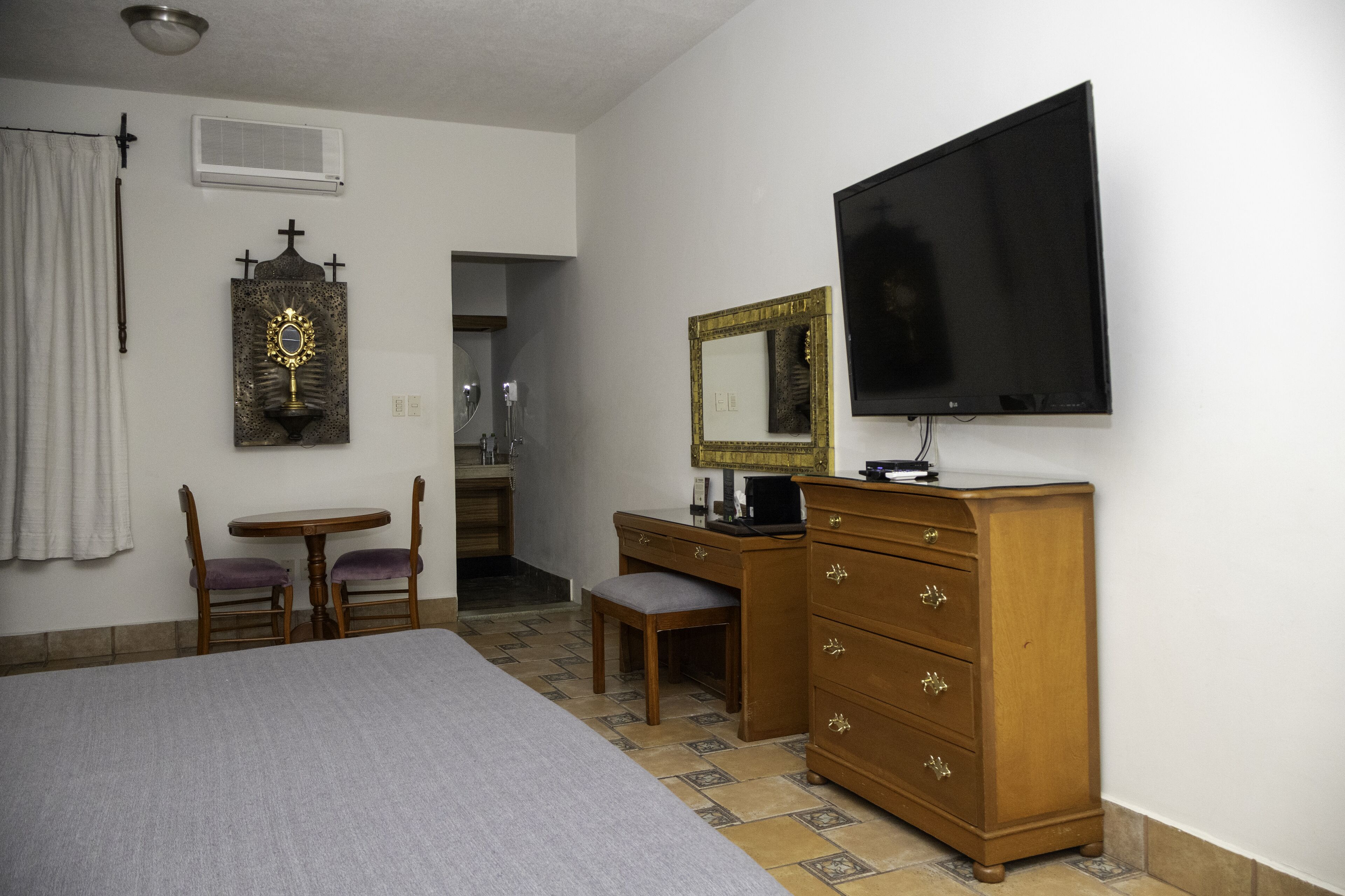 Una habitación de hotel con una cama, un aparador de madera, un escritorio con una silla, un televisor y un espejo.