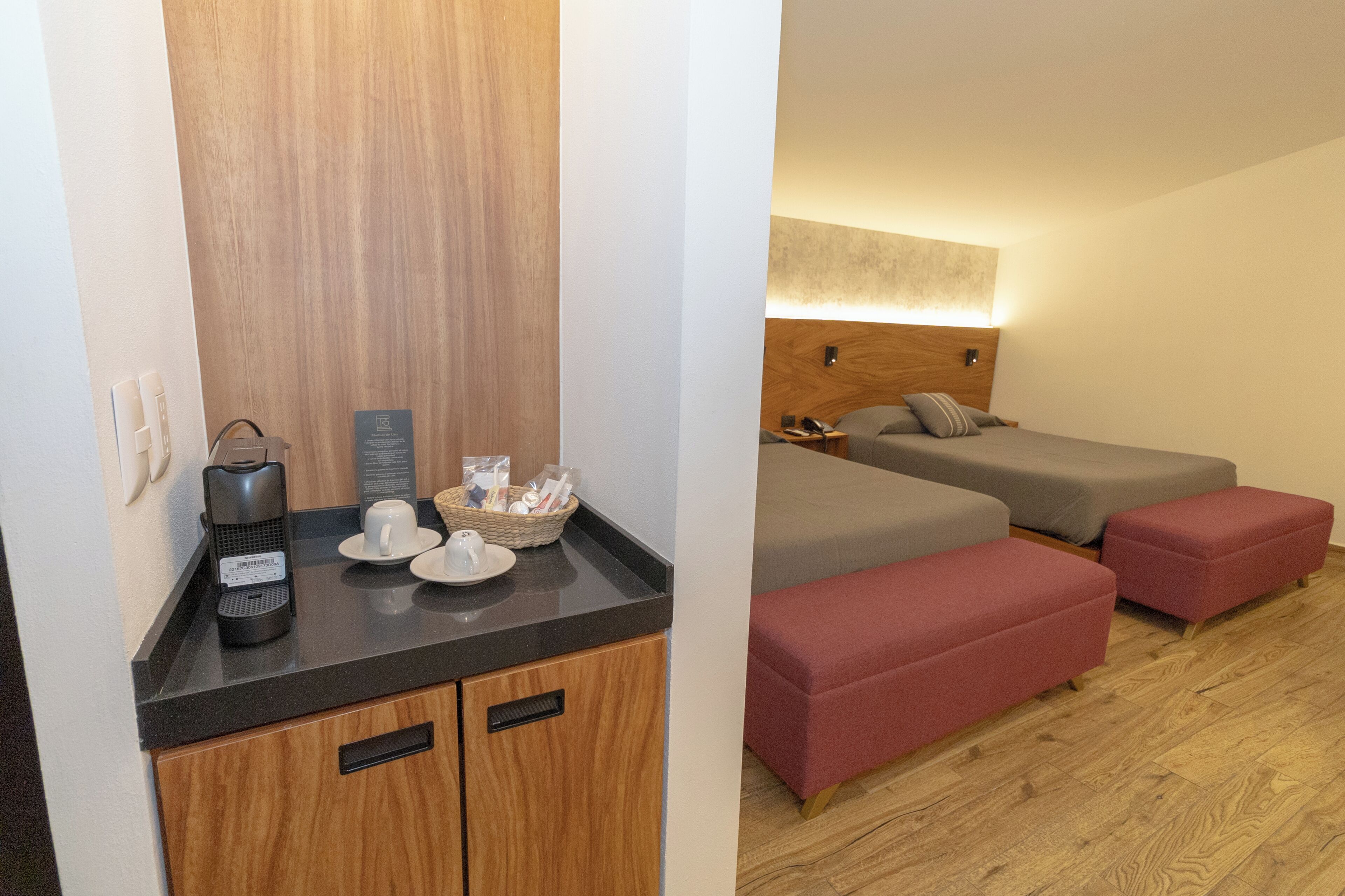 Een hotelkamer met kitchenette, twee bedden met rode voetsteunen, een houten hoofdbord en een wandlamp.
