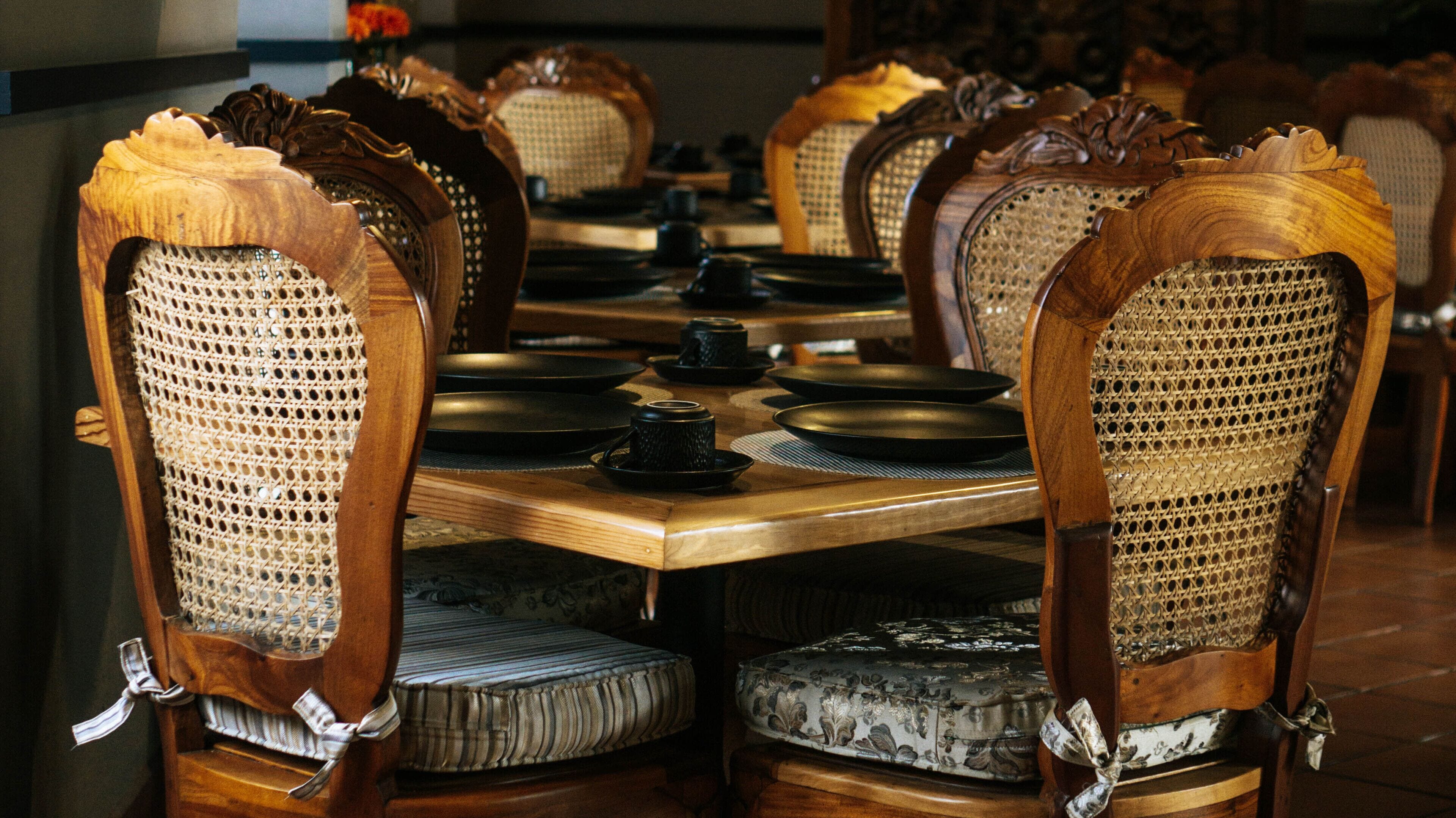 A traditional wooden dining table with ornate chairs, set with plates, bowls, and cups.