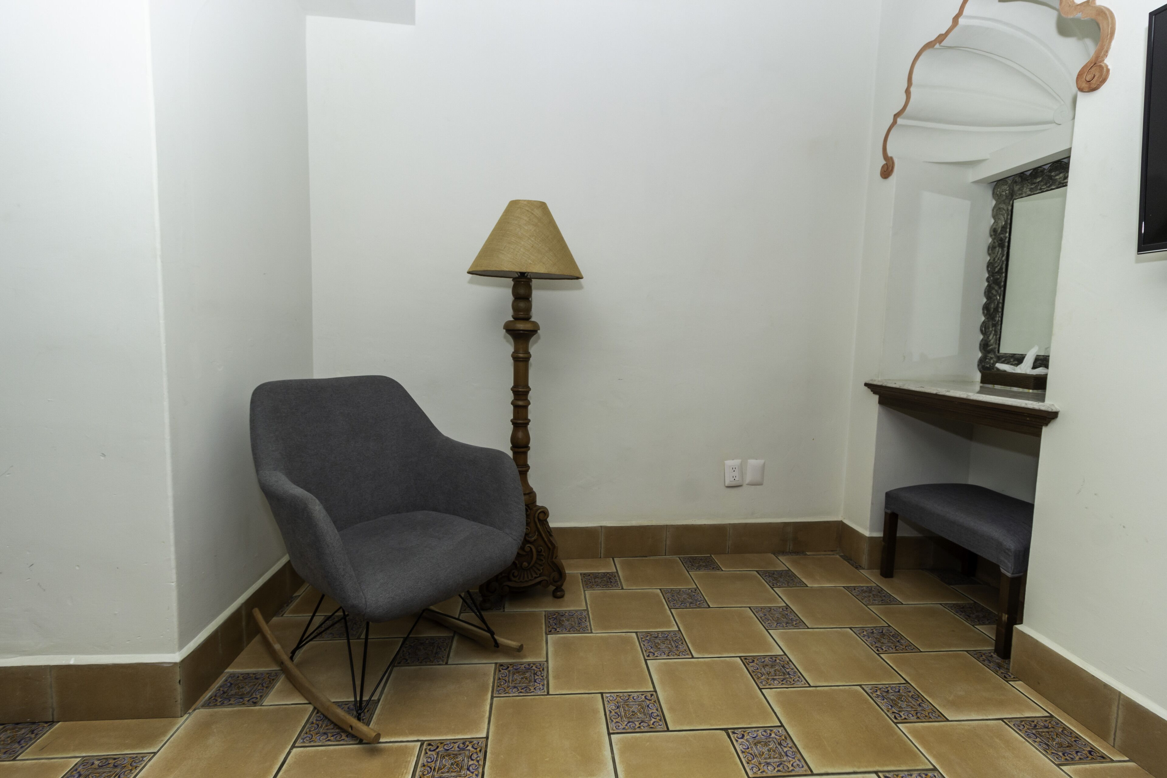 Une pièce d’angle avec une chaise, une lampe, un banc et un miroir au mur.
