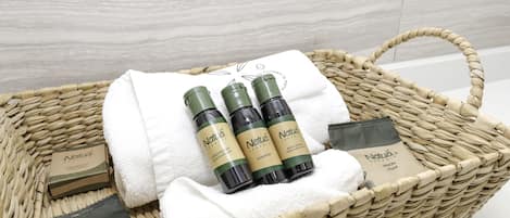 A wicker basket containing three bottles of Natuva organic body care products, a white towel, and a bar of soap.