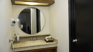 A bathroom with a round mirror, a sink, a towel dispenser, and a hairdryer.