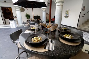 Comedor con mesas redondas, manteles negros y una sombrilla que proporciona sombra.