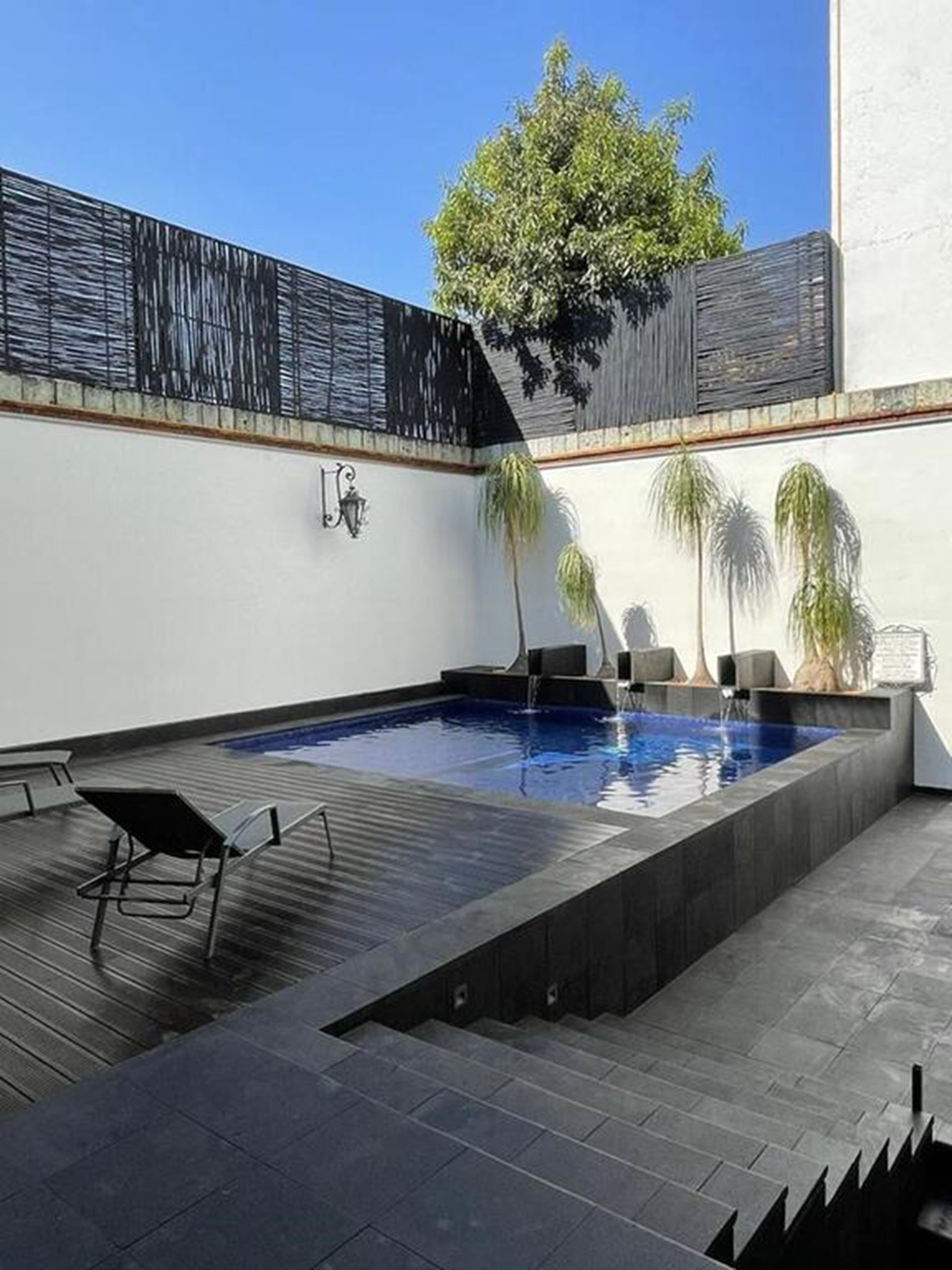 A rooftop pool area with a clear blue sky, a wooden deck, and a few lounge chairs.