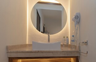 Un baño con un espejo redondo, un lavabo blanco y un secador de pelo montado en la pared.