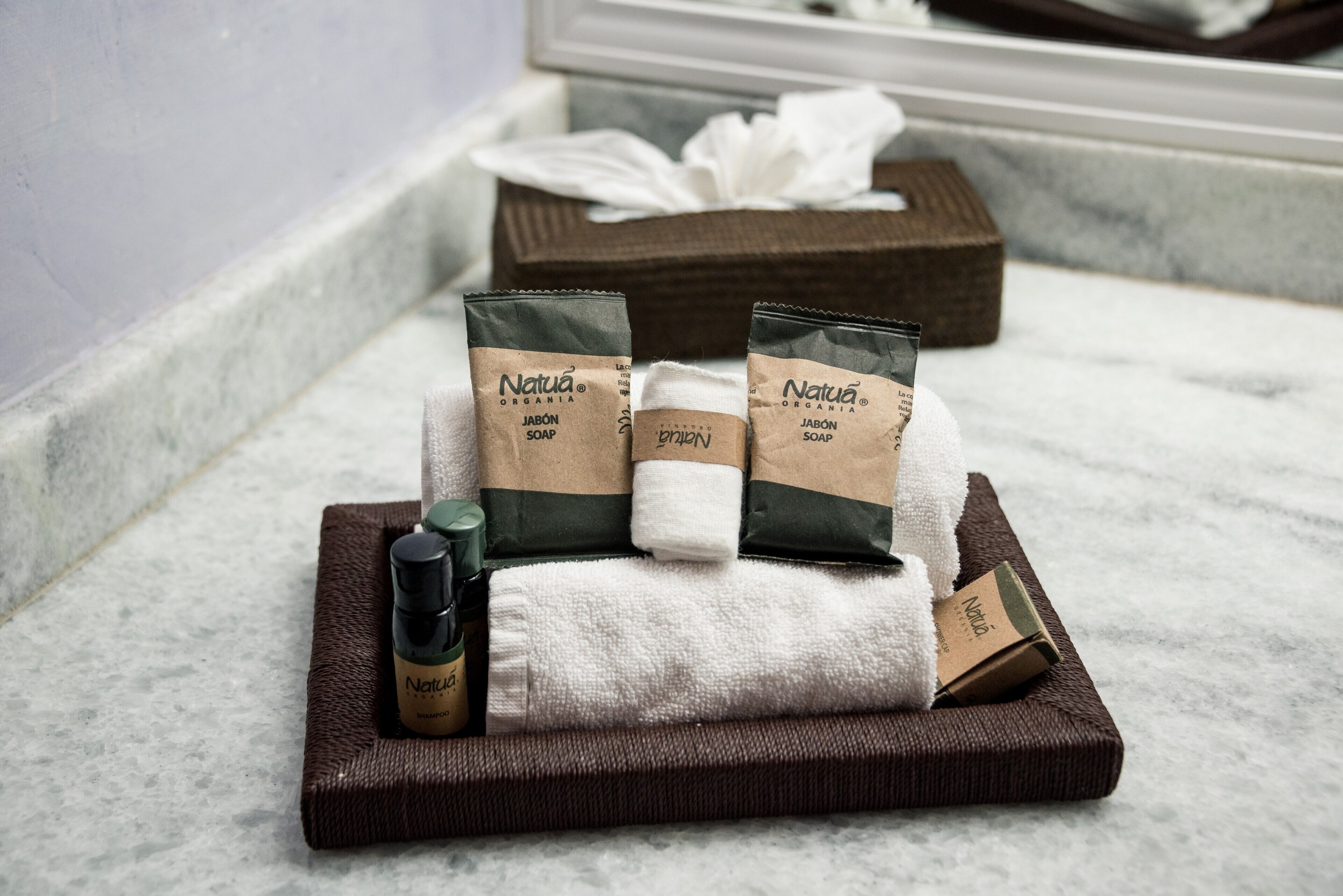 A bathroom with a marble floor, a brown bath mat, a white towel, and two bottles of soap.