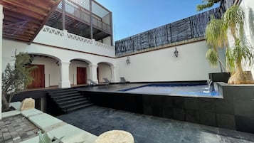 A courtyard with a swimming pool, a covered seating area, and a staircase leading to an upper level.