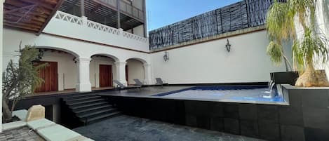 Un patio con piscina, zona de estar techada y una escalera que conduce a un nivel superior.