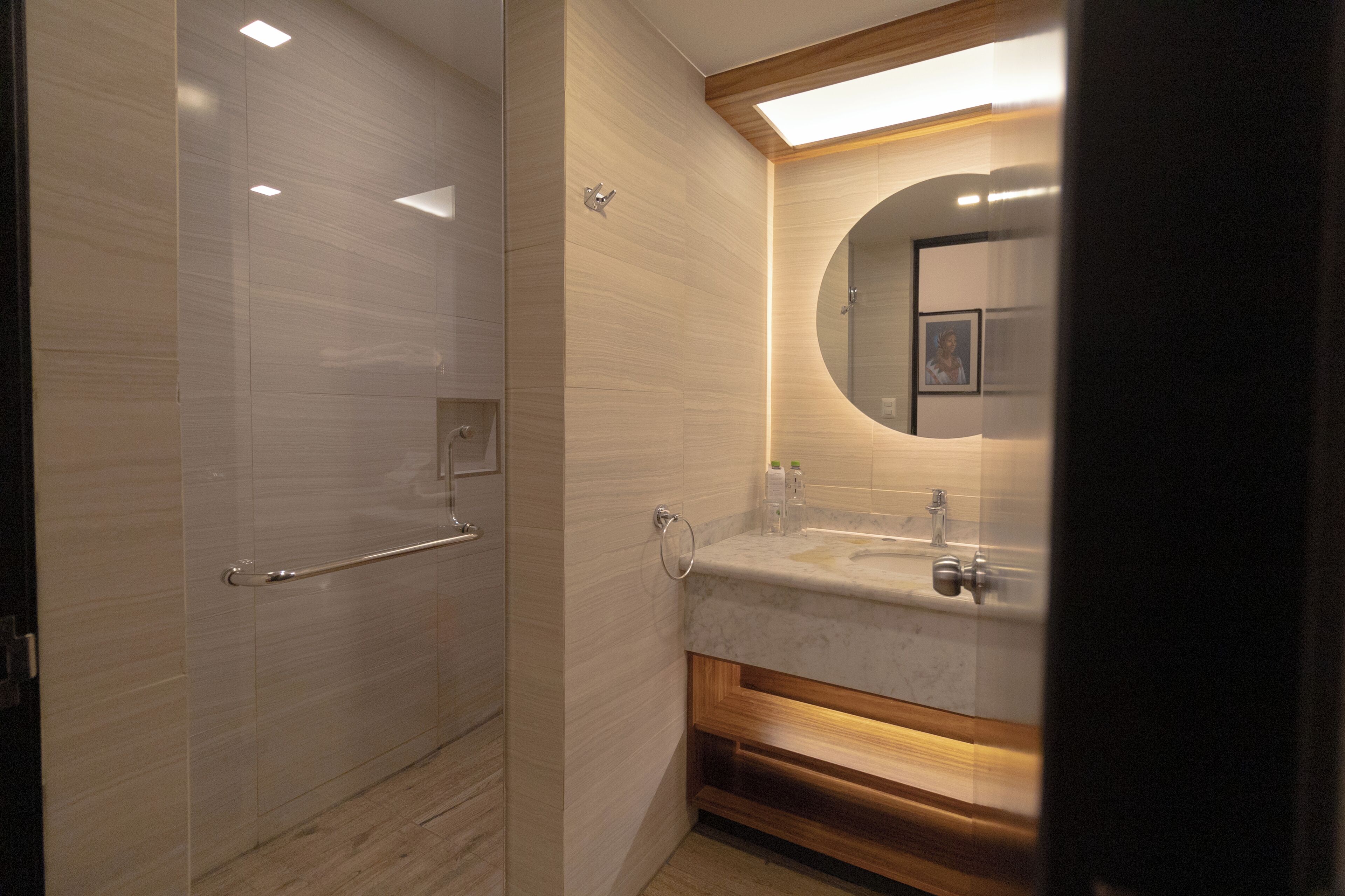 Un baño moderno con cabina de ducha de vidrio, tocador de madera con encimera de mármol y espejo montado en la pared.