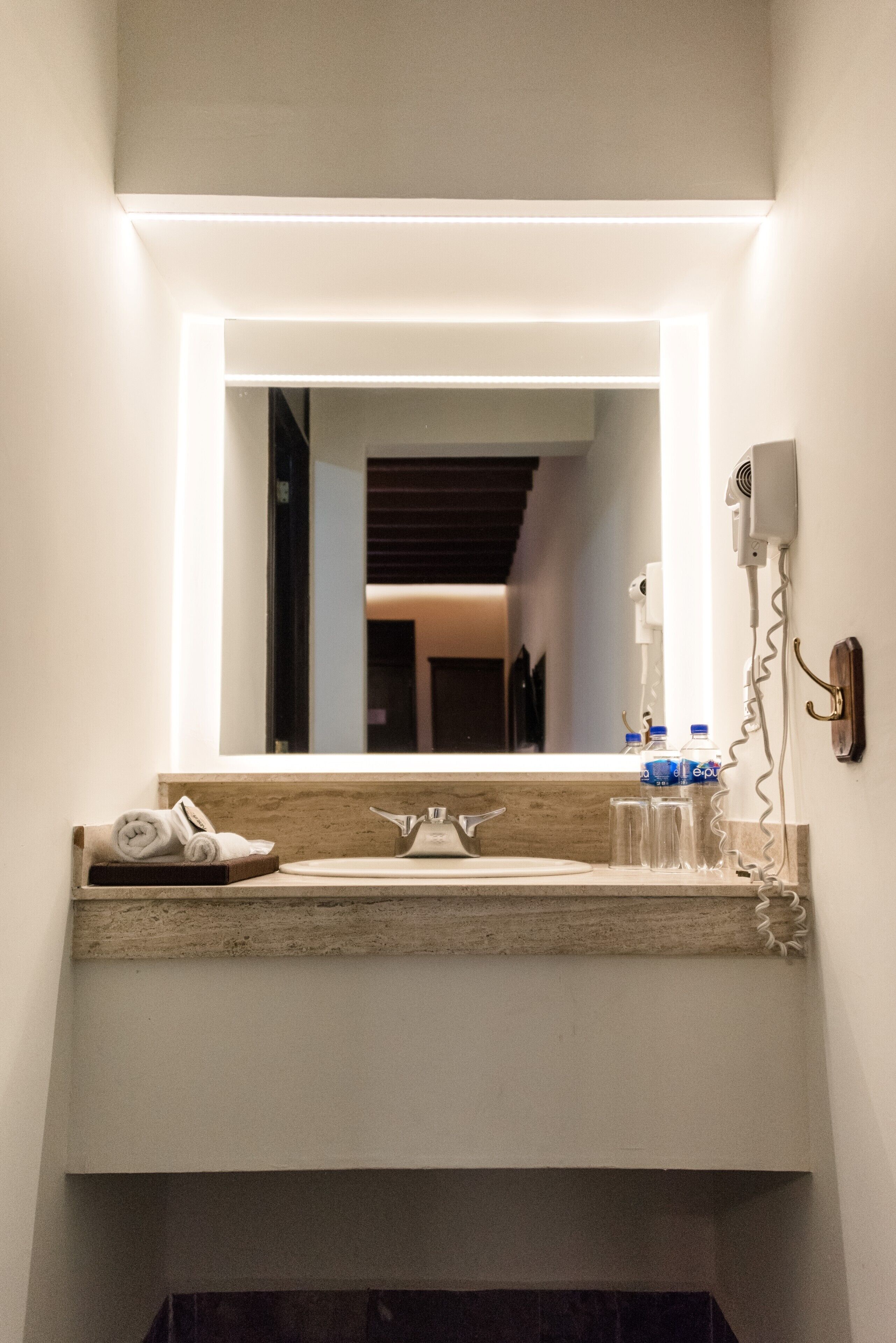 A bathroom with a mirror, sink, towel rack, and a hairdryer on the wall.