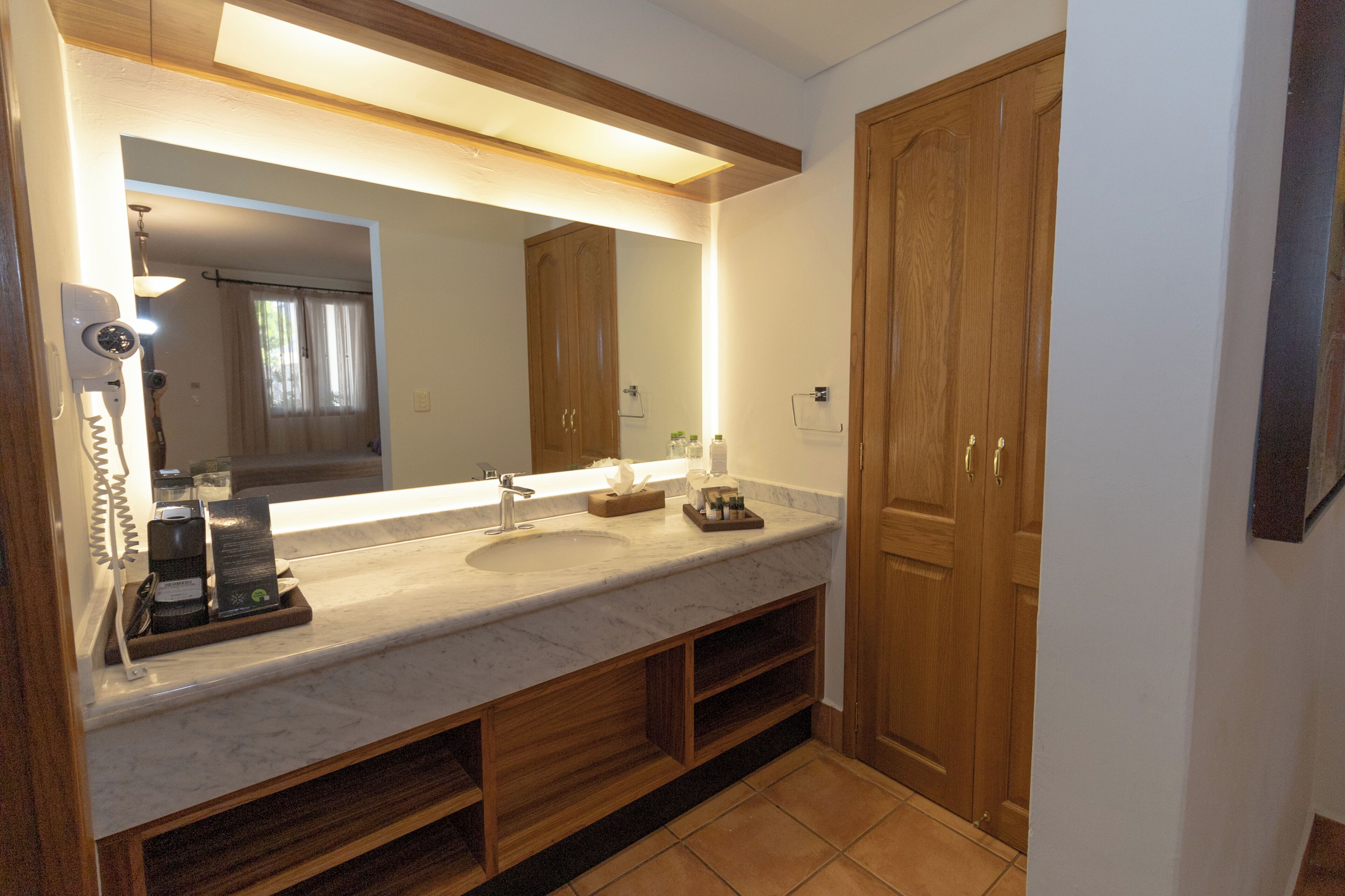 A bathroom with a marble sink, wooden cabinets, a large mirror, and a hairdryer on the counter.