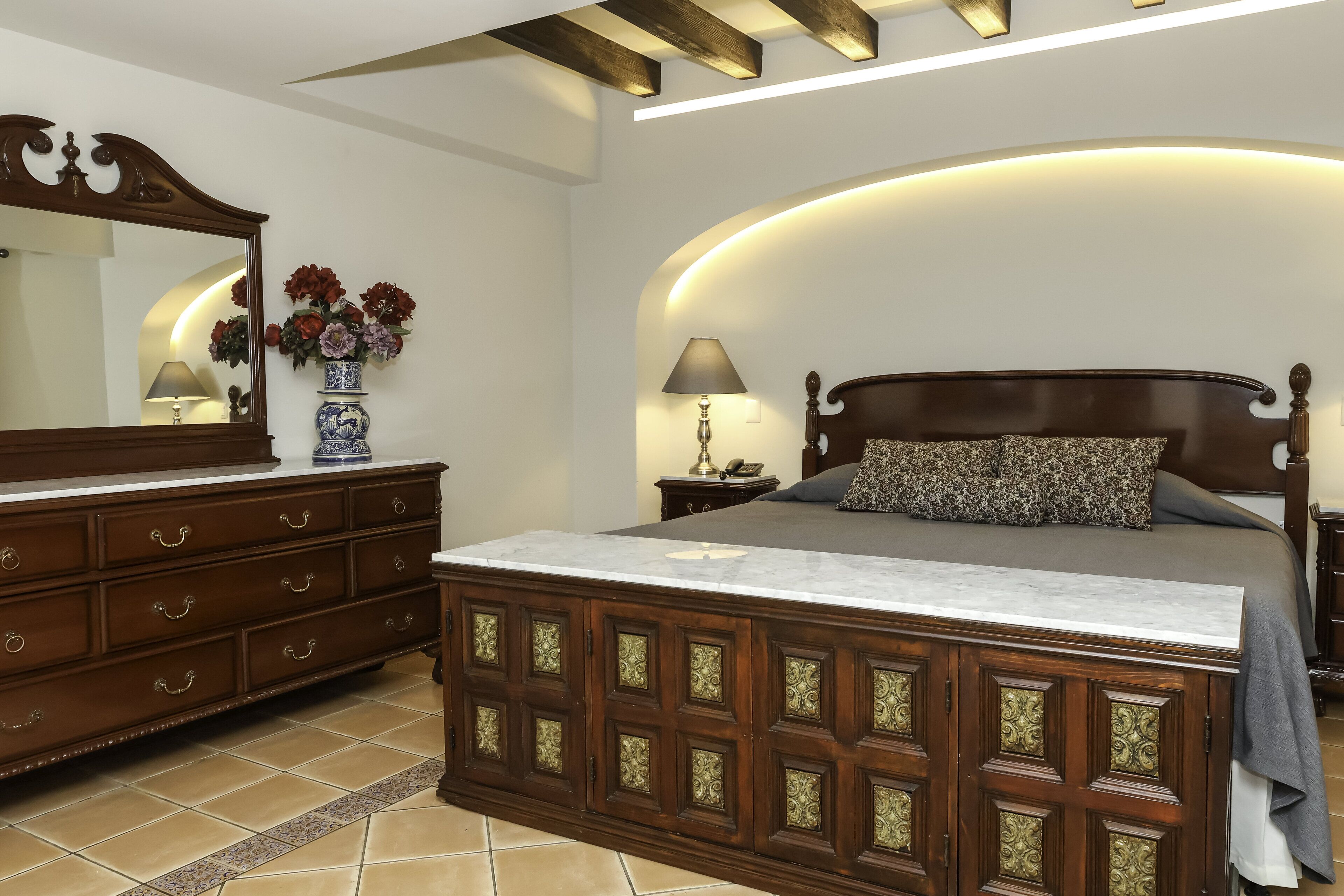 A bedroom with a wooden bed, a dresser, a mirror, and a vase of flowers.