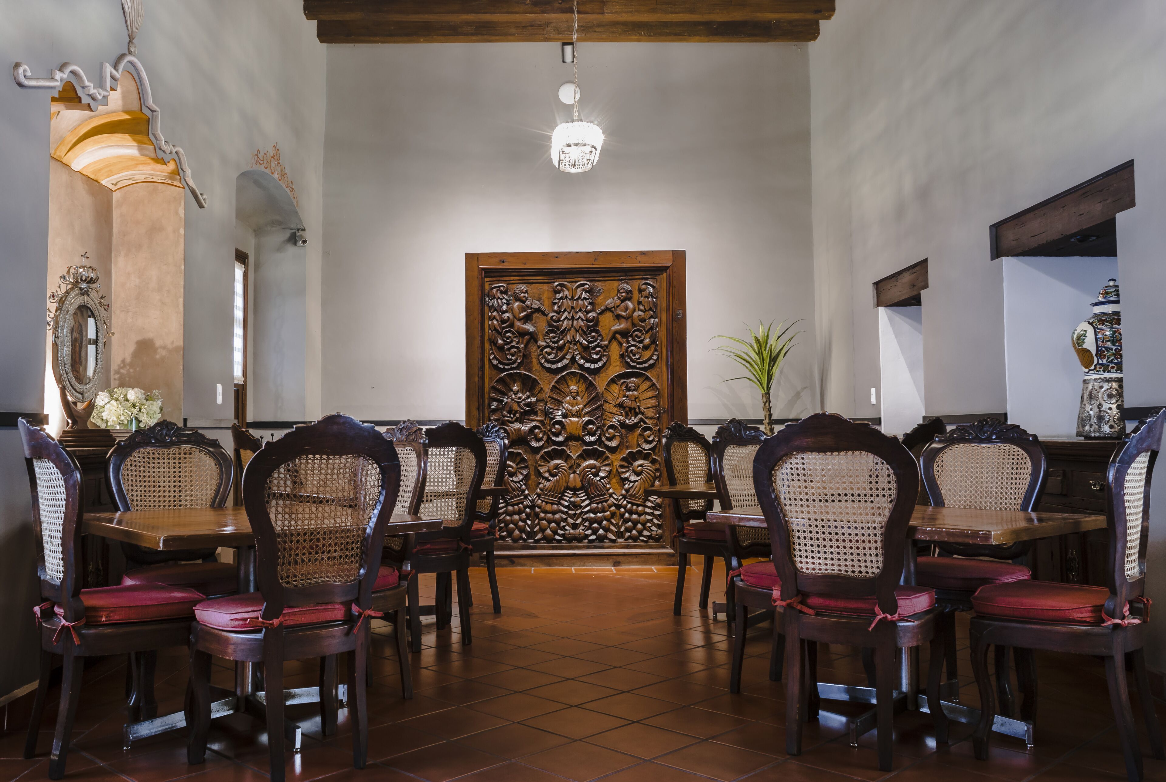 A dining area with wooden tables and chairs, a decorative wall panel, and a chandelier.