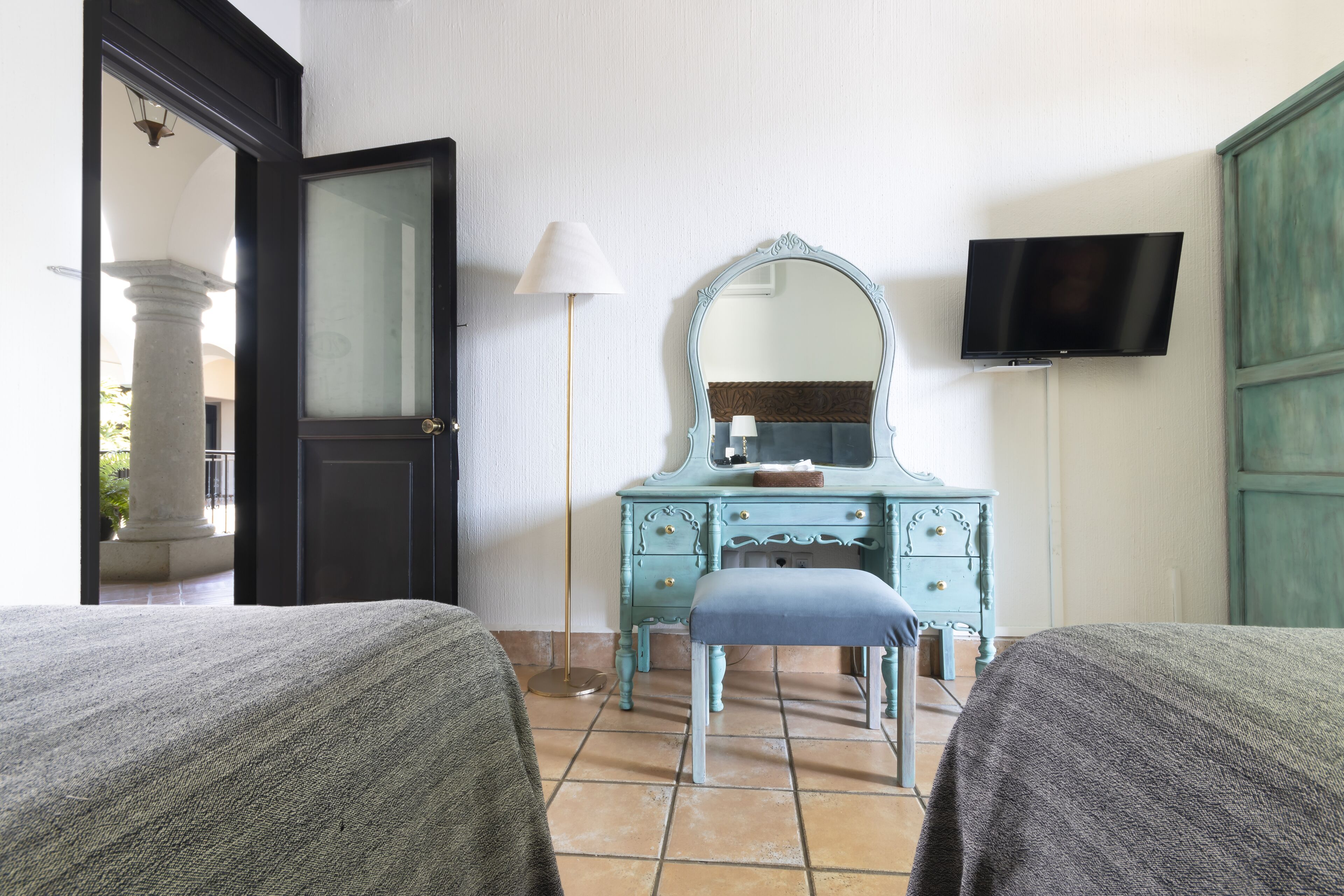 A hotel room with two beds, a dressing table with a mirror, a television, and a lamp.