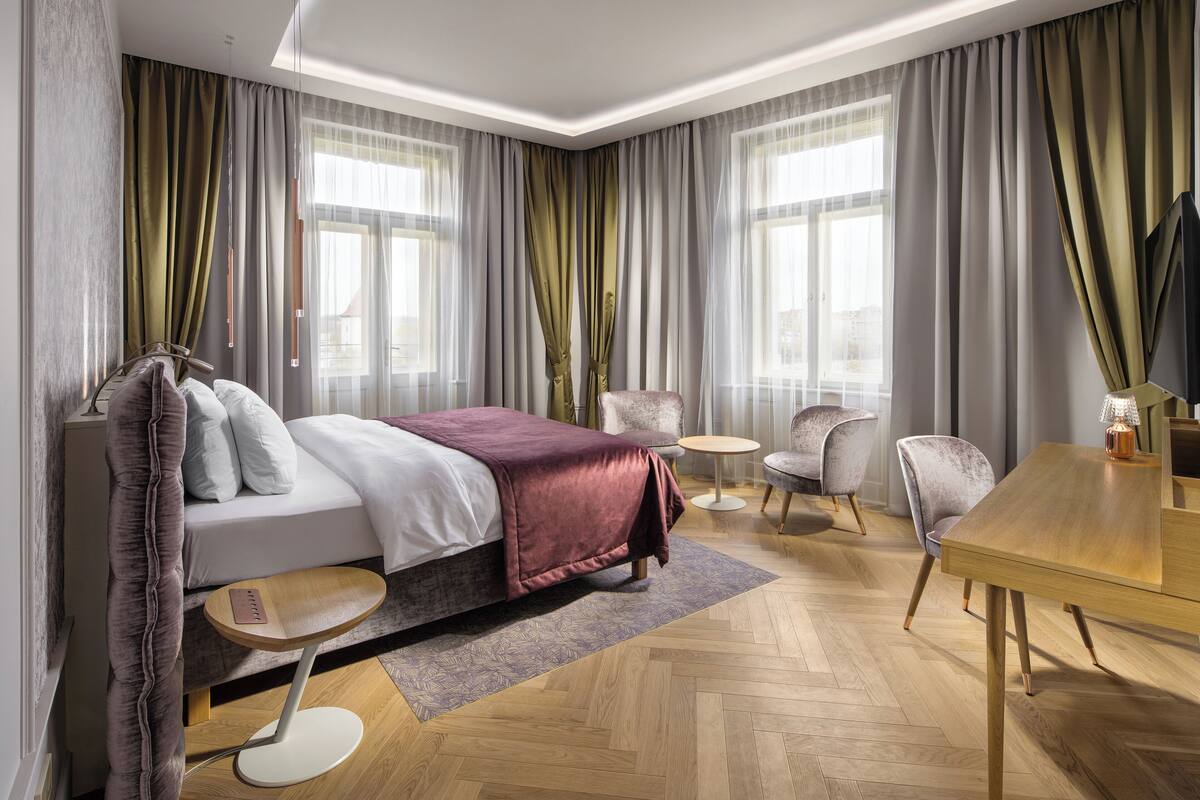 A modern hotel room with a large bed, two armchairs, a small round table, and a wooden dining table.