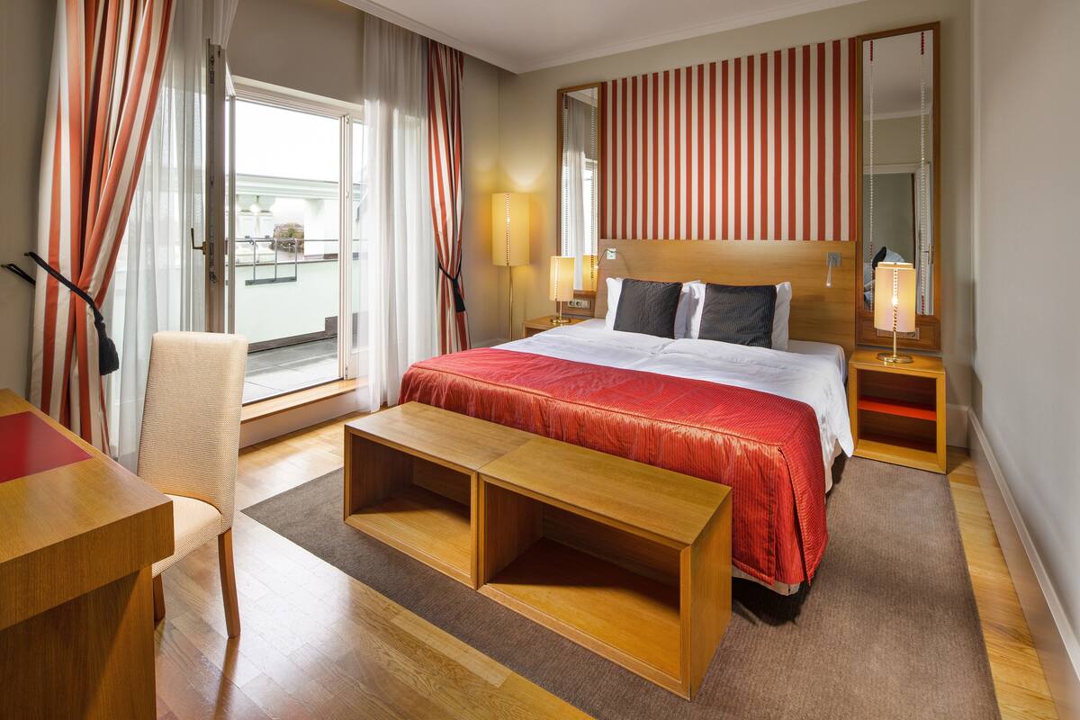 A hotel room with a large bed, a wooden bench, a desk, and a chair.