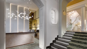 A hotel lobby with a reception desk, a staircase, and a bar area.