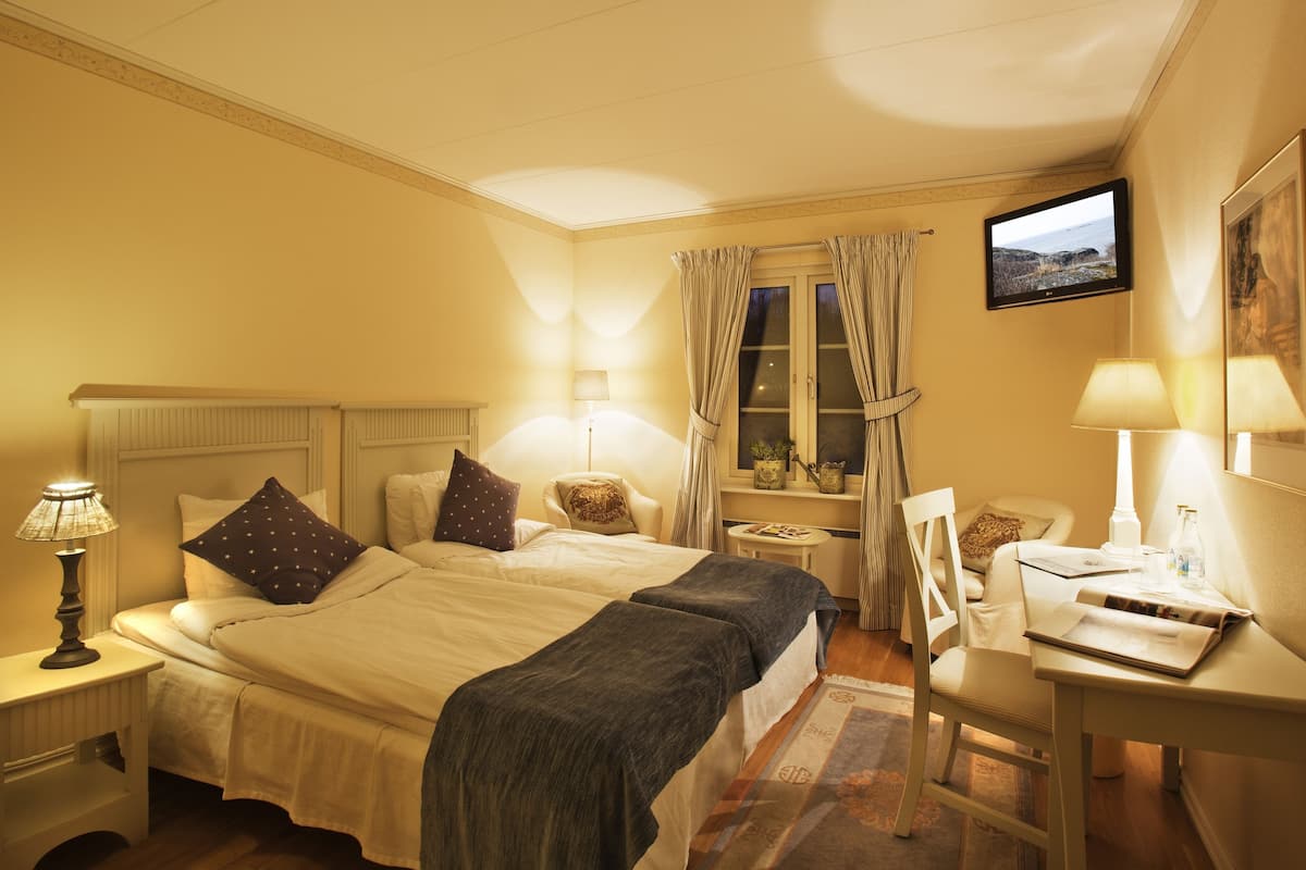 Habitación de hotel con cama, mesitas de noche, escritorio, silla, televisor y ventana con cortinas.