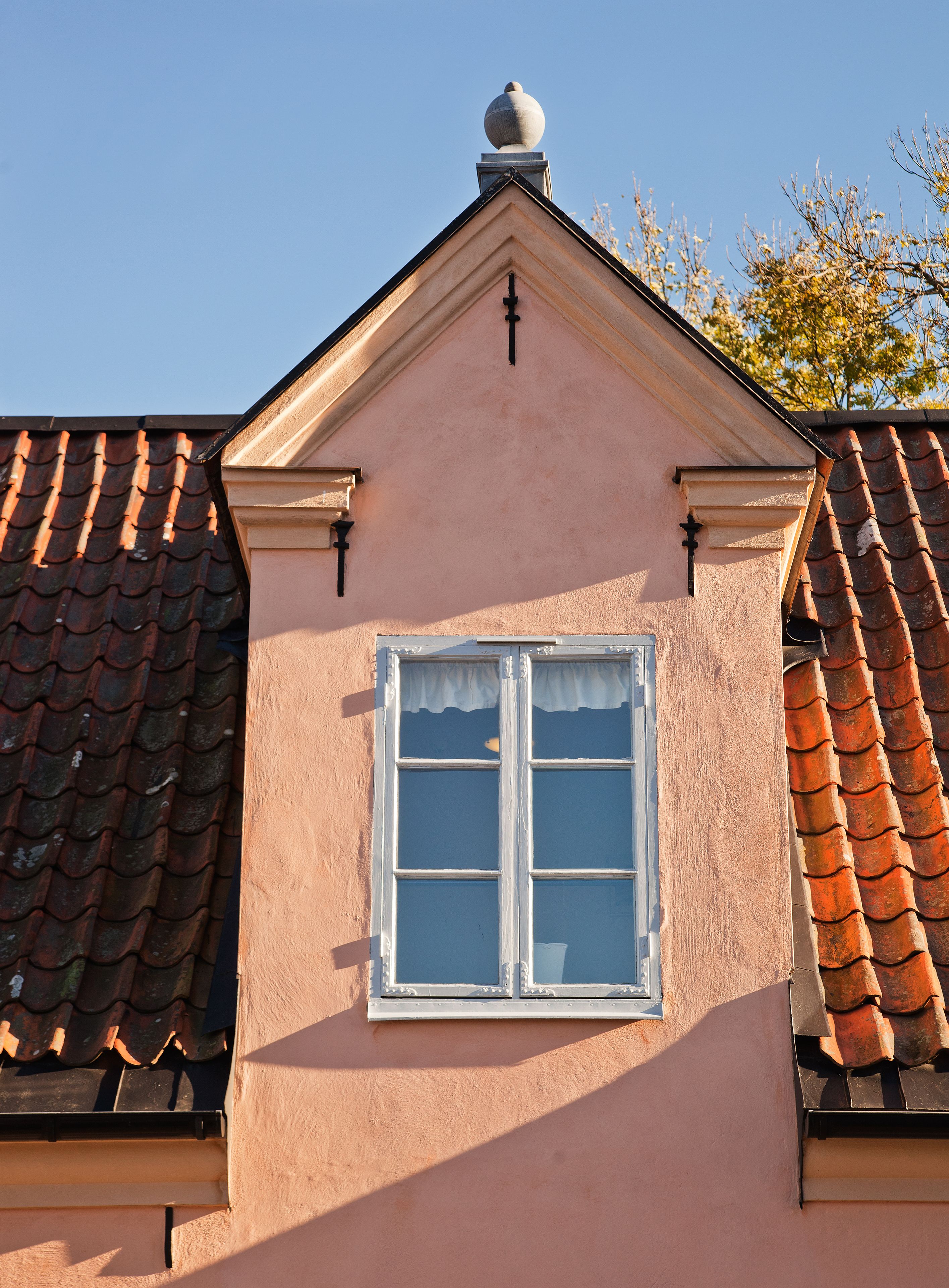 A building with a pink facade, a white window with a white valance, and a tiled roof.
