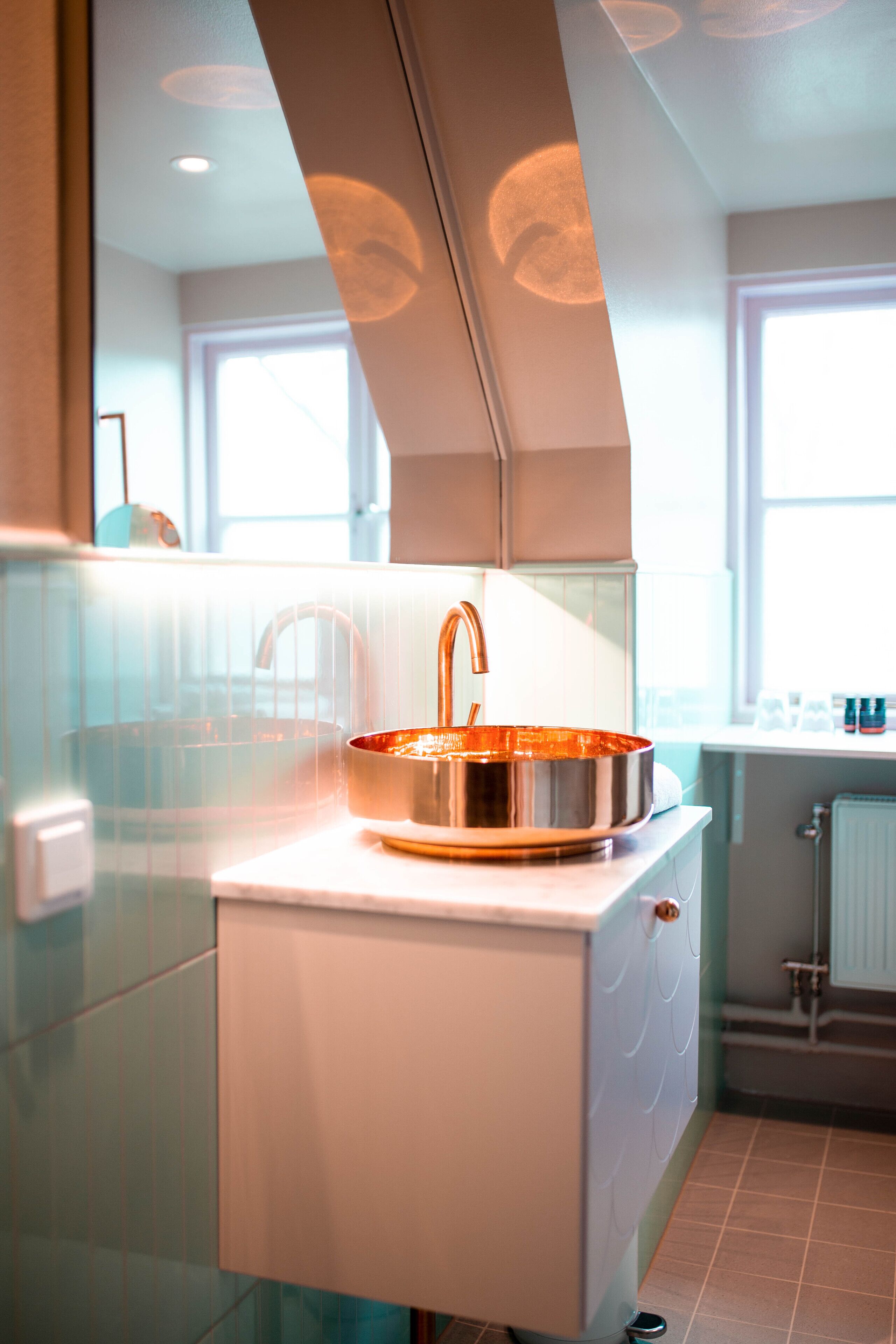 Un bagno moderno con lavandino in rame, uno specchio e una finestra che lascia entrare luce naturale.