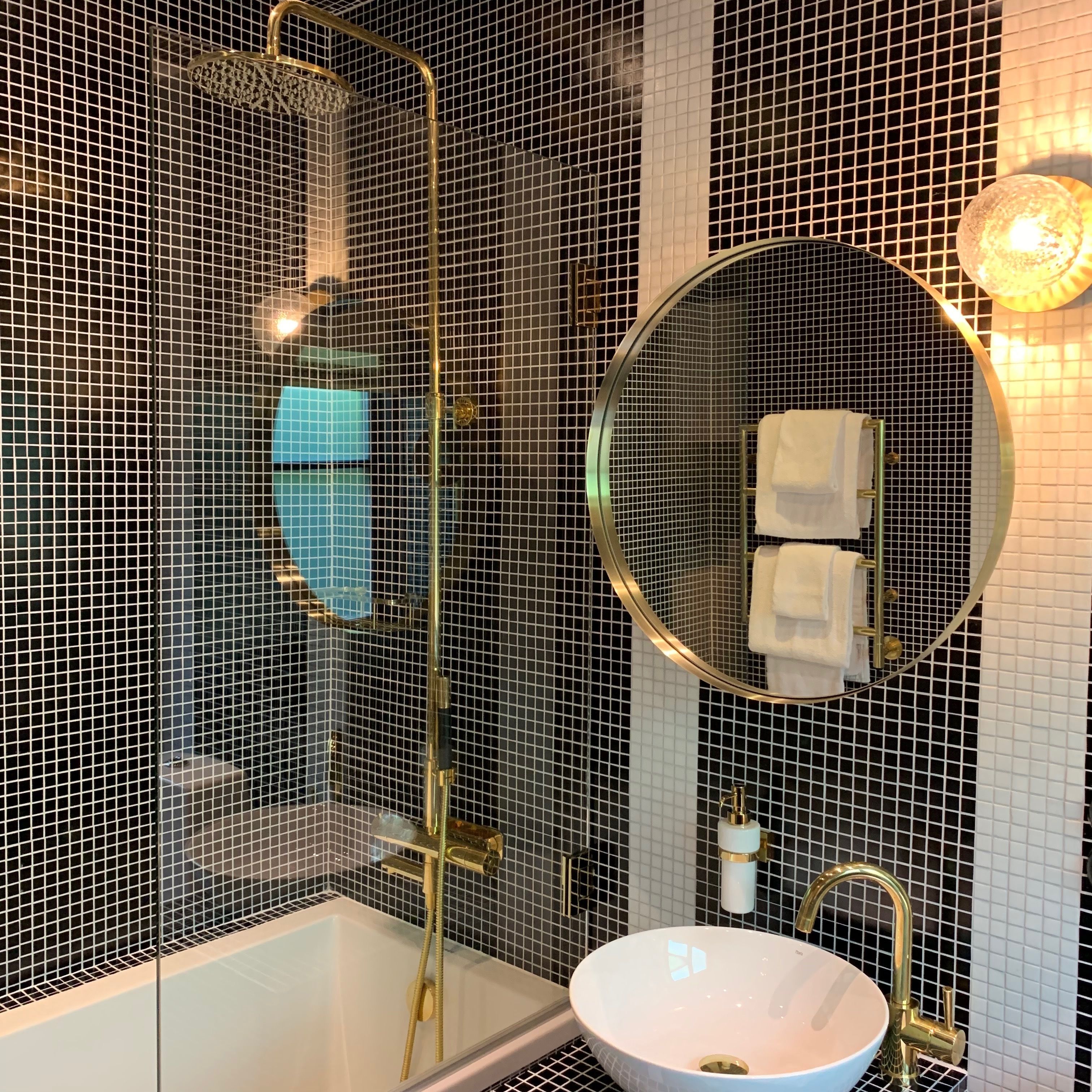 A modern bathroom with a glass-enclosed shower, a round mirror, and a white sink with gold fixtures.