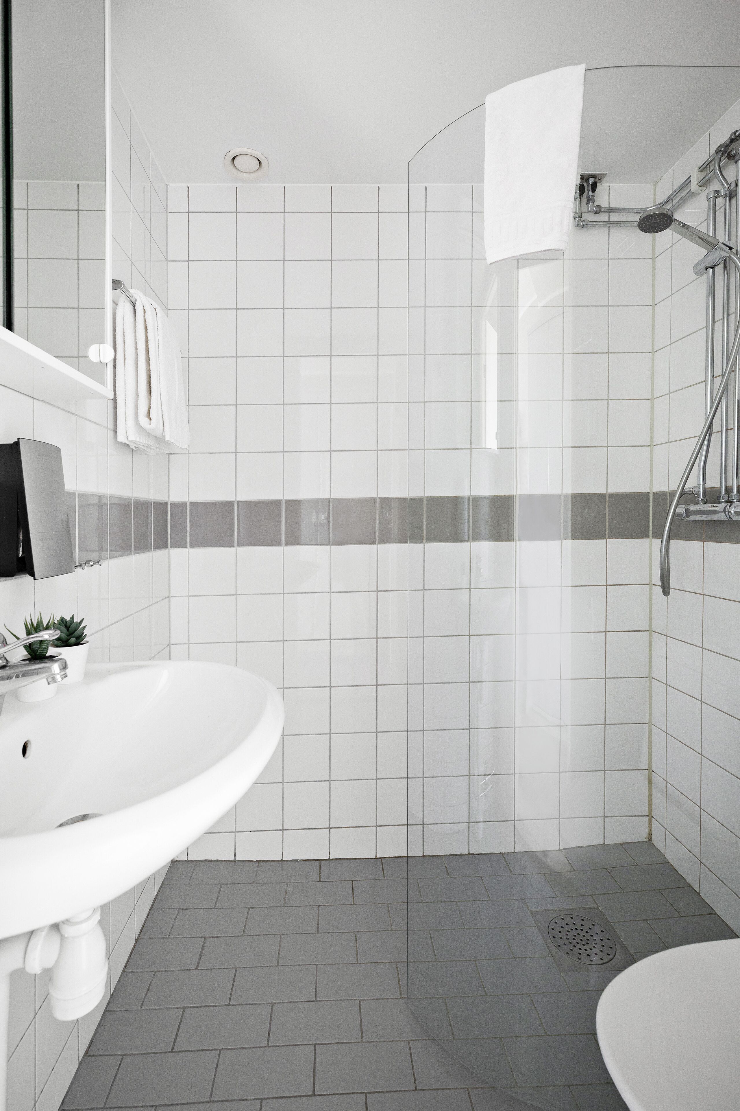 A modern bathroom with a white sink, a shower, and a tiled floor.