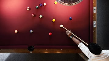 Ein Billardtisch mit roter Spielvliesbahn und eine Person, die ein Queue auf die Kugeln richtet.