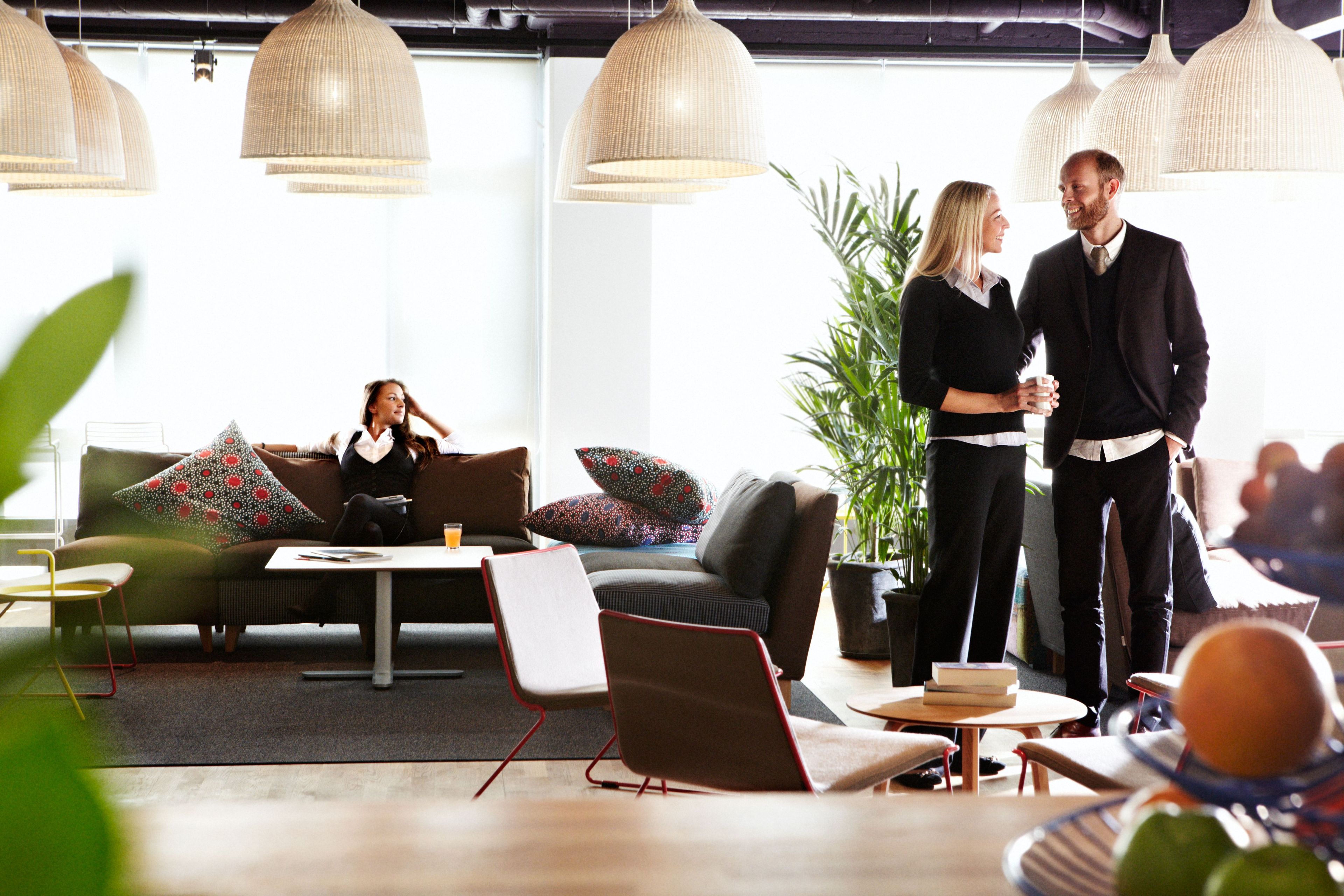 A modern lounge area with comfortable seating, large pendant lights, and a potted plant.