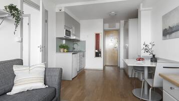 A modern kitchen with white cabinets, a microwave, and a sink. There is a dining area with a table and chairs, and a gray sofa with a striped pillow.
