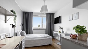 Et moderne soveværelse med seng, skrivebord, stol og et lille spiseområde.