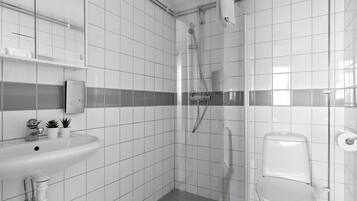 Ein modernes Badezimmer mit weißen Fliesen, einer Duschkabine, einem weißen Waschbecken und einer Toilette.