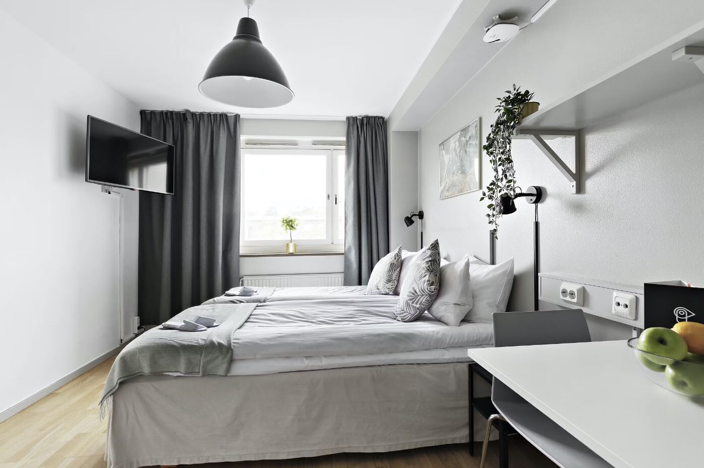 A modern bedroom with a bed, bedside table, desk, and a TV mounted on the wall.
