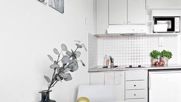 A modern kitchen with white cabinets, a microwave, and a white countertop. There is a vase with a plant on the counter and a plate with apples and a pear.