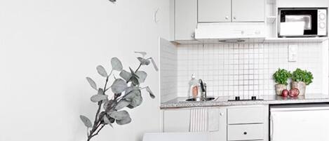 A modern kitchen with white cabinets, a microwave, and a white countertop. There is a vase with a plant on the counter and a plate with apples and a pear.