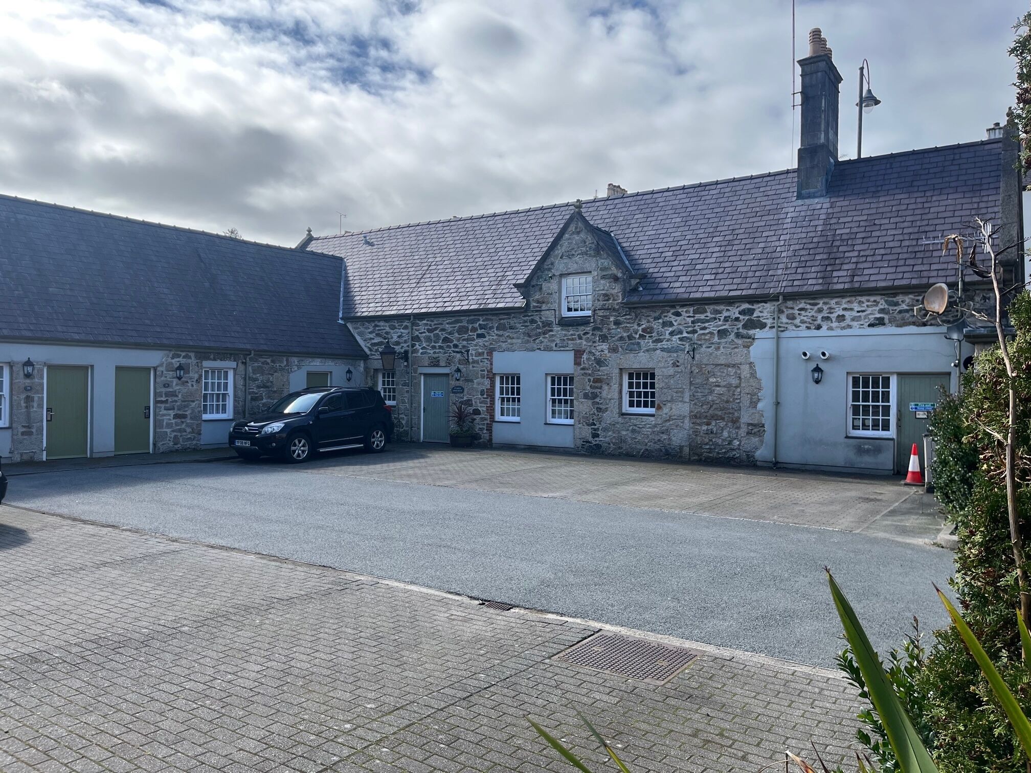 A stone building with a paved driveway and a parked car.