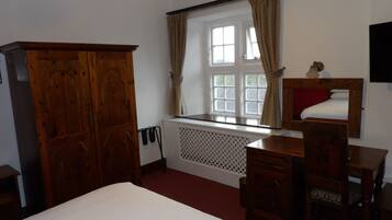 Un dormitorio con una cama grande, un armario de madera, un escritorio con silla, un radiador y una ventana con cortinas.