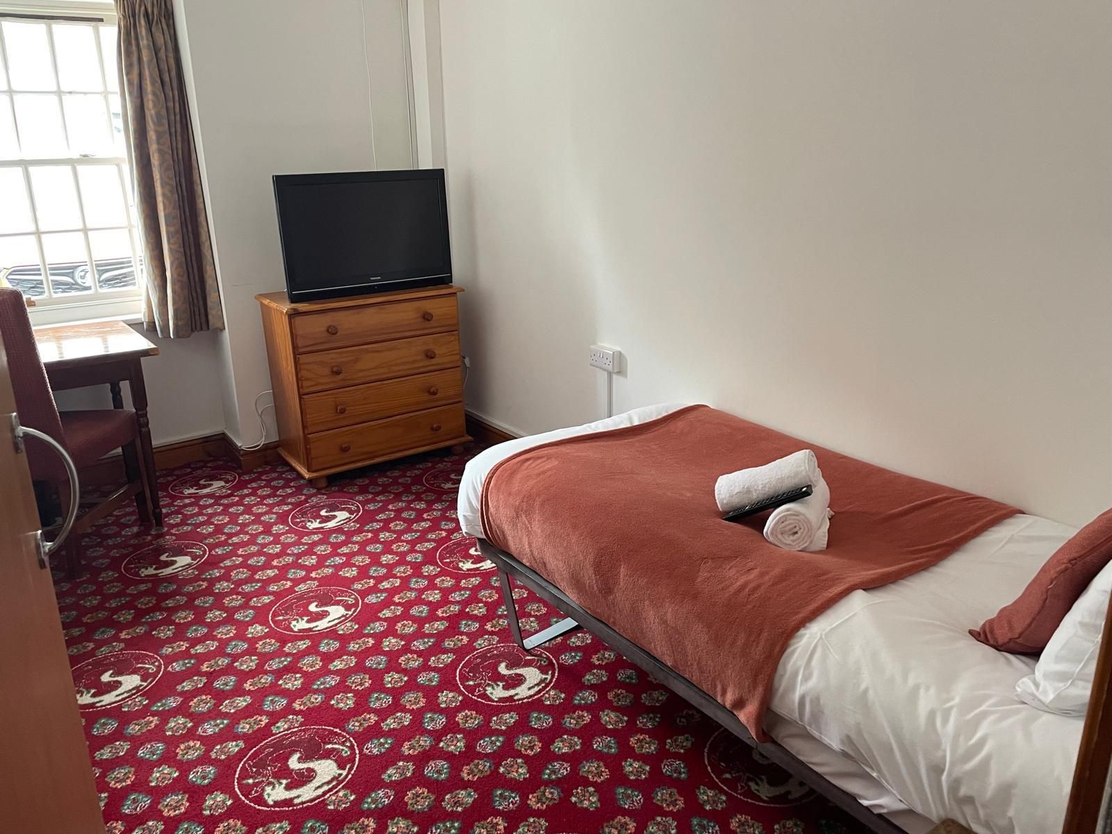 A hotel room with a bed, a dresser, a television, and a window with curtains.