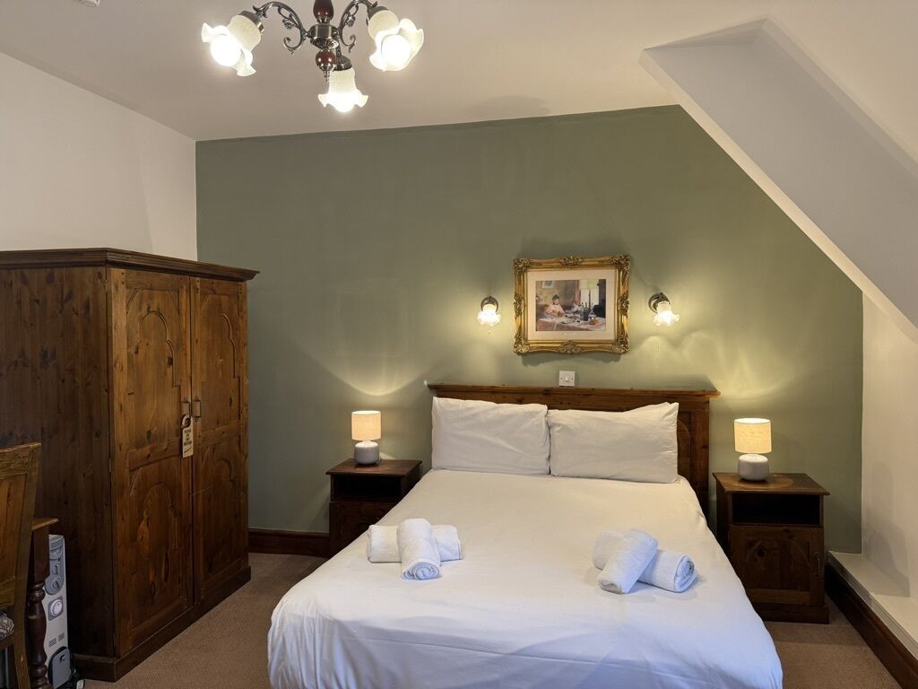 Een slaapkamer met een groot bed, twee bedlampen, een houten garderobe en een kroonluchter.