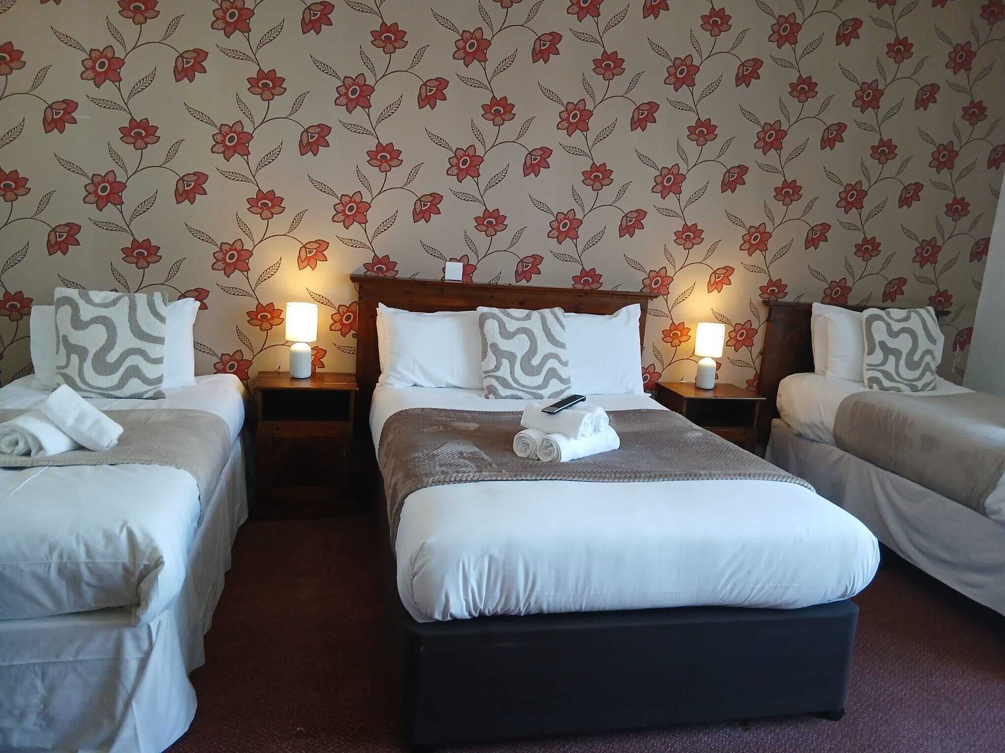 Ein Hotelzimmer mit zwei Einzelbetten, einem Doppelbett und einem Nachttisch mit Lampe.